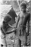 Man ties red cane obi on another man's wrist prior to a feast they are going to give