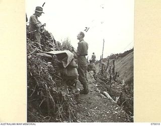 SHAGGY RIDGE, NEW GUINEA. 1944-01-10. PERSONNEL OF THE 2/9TH INFANTRY BATTALION, ALONG A NARROW TRACK CUT INTO THE SIDE OF THE "PIMPLE" WHICH IS OTHERWISE TOO STEEP TO TRAVERSE. THE PHOTOGRAPH ..