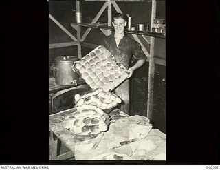 VIVIGANI, GOODENOUGH ISLAND, PAPUA. C. 1943-09. 31979 LEADING AIRCRAFTMAN F. WILLIAMS, COFFS HARBOUR, NSW, DISPLAYS BREAD ROLLS HE HAS BAKED FOR MEMBERS OF NO. 30 (BEAUFIGHTER) SQUADRON RAAF IN NEW ..