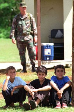 Kurdish children sit near a guard post and a U.S. military guard where they are being temporarily housed after evacuating northern Iraq during PACIFIC HAVEN. The operation, a joint humanitarian effort conducted by the U.S. military, entails the evacuation of over 2,100 Kurds from the northern parts of Iraq to avoid retaliation from Iraq for working with the U.S. government and international agencies. The refugees are awaiting immigration process to become United States residents