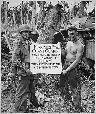 The U.S. Marines salute the U.S. Coast Guard after the fury of battle had subsided and the Japanese on Guam had been defeated. "They (the Coast Guard) Put Us Here and We Intend to Stay" is the way the Marines felt about it.