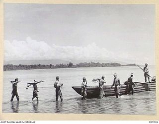 JAPANESE TROOPS LOAD A BARGE WITH EQUIPMENT FOR DUMPING AT SEA, IN ACCORDANCE WITH SURRENDER ARRANGEMENTS MADE WITH THE AUSTRALIAN SURRENDER PARTY FROM HEADQUARTERS 2 CORPS WHO ARRIVED AT NUMA NUMA ..