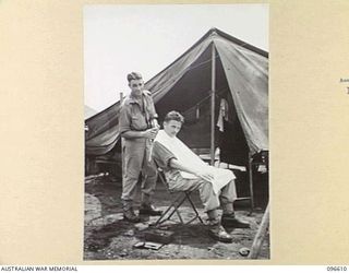 CAPE WOM, WEWAK AREA, NEW GUINEA. 1945-09-15. PRIVATE J.D. ROCHE (1), GIVING PRIVATE D.D. D'ARCY (2) A HAIRCUT AT HEADQUARTERS 6 DIVISION