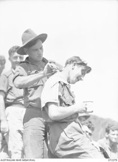 YAULA, NEW GUINEA. 1944-04-09. VX146009 PRIVATE MCMAHON (3), RECEIVES A HAIRCUT FROM VX142336 PRIVATE LEVENS (2), WITH VX81105 LIEUTENANT A.J. MELLETT (1) AT THE BACKGROUND. THE HAIRCUT IS TAKING ..