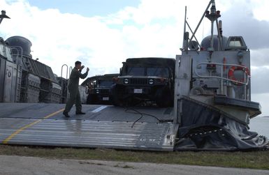 A US Navy (USN) crewmember on board a USN Landing Craft, Air Cushioned (LCAC) directs a US Marine Corps (USMC) High-Mobility Multipurpose Wheeled Vehicle (HMMWV) on to the beach at Inner Apra Harbor, Guam. The LCAC along with its support ship is here to participate in Exercise TANDEM THRUST 2003