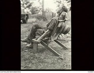 VIVIGANI, GOODENOUGH ISLAND, PAPUA. C. 1944. LEADING AIRCRAFTMAN A. GREEN RAAF RELAXES IN A CHAIR WHICH GREW OUT OF A JEEP WINDSCREEN FRAME AND SUNDRY PIECES OF TIMBER