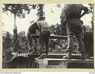 BOUGAINVILLE. 1945-04-18. 15 FIELD COMPANY ROYAL AUSTRALIAN ENGINEERS SAPPERS LAYING HEAVY DECKING ON TO BOX GIRDERS DURING THE CONSTRUCTION OF A 25-TON BRIDGE OVER DAWE CREEK
