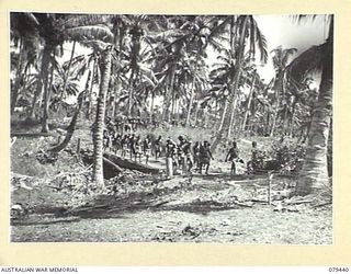 RIFE AREA, NEW BRITAIN. 1945-03-06. SOME OF THE 280 AUSTRALIAN NEW GUINEA ADMINISTRATIVE UNIT NATIVE CARRIERS MOVING THROUGH THE VILLAGE AFTER EVACUATING THEIR FORWARD CAMP WHICH WAS SUBJECTED TO A ..