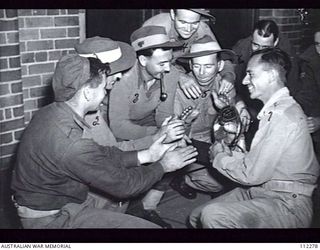 SYDNEY, NSW. 1 AUGUST 1945. A GROUP OF 5 YEAR VETERANS, RETURNED HOME FRESH FROM BOUGAINVILLE, GATHERED ROUND THE RADIATOR WHILE THEY WAIT FOR THEIR MEDICAL EXAMINATION BEFORE THEY GO ON DISCHARGE ..