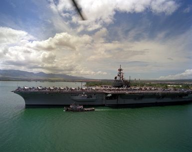 Sailors man the rails aboard the aircraft carrier USS RANGER (CV-61) as the large harbor tug WAXAHATCHIE (YTB-814) escorts the vessel in preparation for assisting it in docking. The RANGER is stopping off at Pearl Harbor while en route to its home port after returning from deployment in the Persian Gulf during Operation Desert Storm