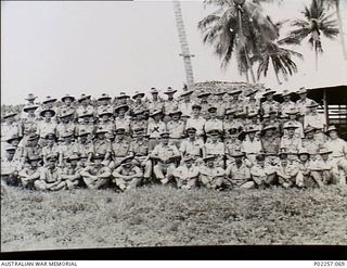 Madang, New Guinea, 1944-12-25. Outdoors group portrait of members of the Officers' Mess, Headquarters, RAAF Northern Command (NORCOM), on Christmas Day. Sitting in the centre of the group with ..