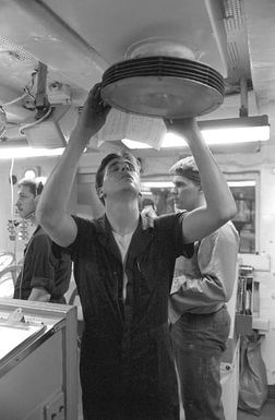 A sailor in an engineering space aboard the amphibious assault ship USS SAIPAN (LHA-2) uses a sheet of paper to direct cool air from a vent onto his face as preparations are made to shut down one of the ship's boilers for maintenance. The SAIPAN steamed at flank speed for a week to be on station off the coast of Liberia for OPERATION SHARP EDGE