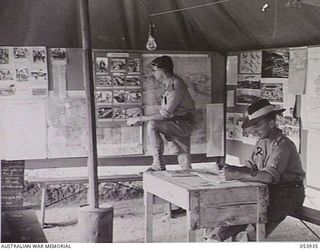 KOITAKI, NEW GUINEA. 1943-07-13. AUSTRALIAN ARMY EDUCATION SERVICE WALL NEWSPAPER ON DISPLAY IN A HUT AT THE PORT MORESBY AREA EDUCATION CENTRE. SHOWN ARE: QX42598 CAPTAIN H. COPPOCK, DEPUTY ..