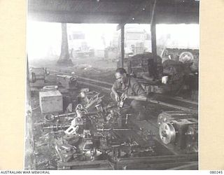 HANSA BAY AREA, NEW GUINEA. 1944-07-10. A MEMBER OF 5TH DIVISION SALVAGE GROUP WORKING ON HEADSTOCKS, TAILSTOCKS AND SADDLES OF ABANDONED JAPANESE LATHE EQUIPMENT. EACH LATHE IS CURRENTLY VALUED AT ..