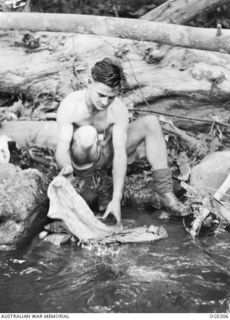 TSILI TSILI, PAPUA NEW GUINEA. 1943-11-18. FLIGHT SERGEANT M. J. BROWN OF SCONE, NSW, A MEMBER OF NO. 4 (ARMY CO-OPERATION) SQUADRON RAAF, WASHING HIS CLOTHES IN A JUNGLE STREAM