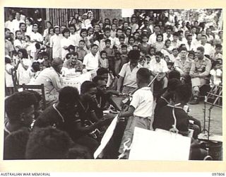 RATONGOR, NEW BRITAIN. 1945-10-10. SMALL CHINESE BOYS OFFERING REFRESHMENTS BETWEEN NUMBERS TO MEMBERS OF THE ROYAL PAPUAN CONSTABULARY BAND. THE BAND PLAYED FOR THE GALA DAY CELEBRATIONS HELD AT ..