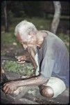 Carving: older man uses an adze with metal blade to shape a piece of wood