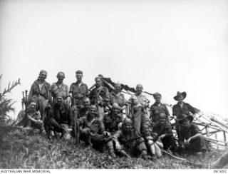 WAREO, NEW GUINEA. 1943-12-09. OFFICERS AND MEN OF A COMPANY, 2/23RD AUSTRALIAN INFANTRY BATTALION, PHOTOGRAPHED IN FRONT OF THE BOMB SHATTERED MISSION BUILDINGS. SHOWN ARE: VX58466 PRIVATE F. E. ..