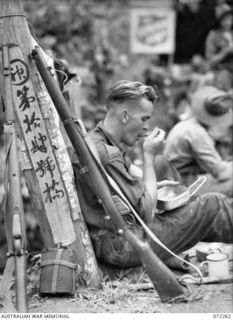 DUMPU, NEW GUINEA. 1944-04-03. VX109943 CORPORAL T.R. JAMES, 15TH FIELD COMPANY, ROYAL AUSTRALIAN ENGINEERS, HAVING LUNCH ON A BRIDGE WITHIN FIVE MILES OF BOGADJIM WHILE RESTING AGAINST A JAPANESE ..