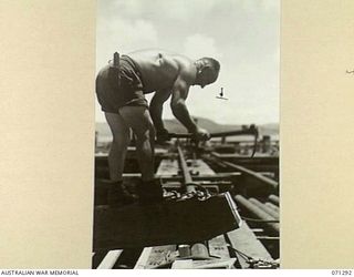 PORT MORESBY, PAPUA, 1944-03-21. VX31032 LANCE-CORPORAL C.G. GREEN (1), OF THE 2/16TH FIELD COMPANY, ROYAL AUSTRALIAN ENGINEERS, TRIMMING A BRACING BEAM USED FOR WHARF SUPPORT IN THE CONSTRUCTION ..