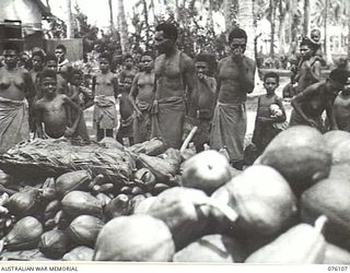 KARKAR ISLAND, NEW GUINEA. 1944-10-20. NATIVES ALONGSIDE TROPICAL FRUIT GATHERED FOR THE AUSTRALIAN NEW GUINEA ADMINISTRATIVE UNIT FOR DISTRIBUTION TO TROOPS ON THE MAINLAND