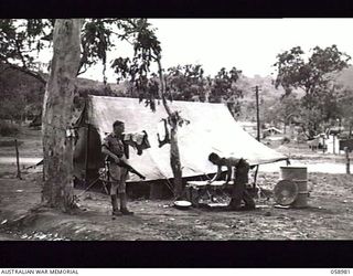 NEW GUINEA. 1943-10. TX1716 SERGEANT F. R. MUSSON (WITH RIFLE) OUTSIDE HIS TENT AT THE AUSTRALIAN MILITARY HISTORY SUBSECTION CAMPSITE HEADQUARTERS, NEW GUINEA FORCE