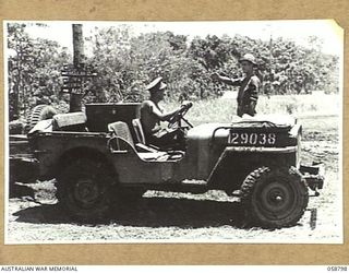 DUMPU, NEW GUINEA, 1943-10-10. MILITARY POLICEMAN, NX154530 CORPORAL R.A. HARGREAVES (RIGHT) OF THE 7TH AUSTRALIAN DIVISION PROVOST COMPANY DIRECTING A JEEP BY THE SIGNPOST IN THE RAMU VALLEY