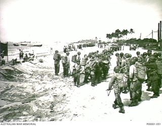 THE SOLOMON ISLANDS, 1945-01-13. AFTER LANDING, TROOPS MUSTER ON A BOUGAINVILLE ISLAND BEACH AS MORE LANDING CRAFT APPROACH WHILST OTHERS SHUTTLE BACK TO SHIPS OFFSHORE. (RNZAF OFFICIAL PHOTOGRAPH.)