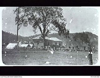 PORT MORESBY, NEW GUINEA. 1914-08. INSCRIPTION ON VERSO: "DIGGING TRENCHES, RADIO STATION, PORT MORESBY, AUG 1914". NATIVES DIG INSIDE THE BARBED WIRE PERIMETER FENCE, WITH SANDBAGS MARKING THE ..