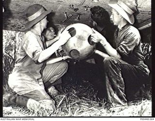 BOUGAINVILLE, PNG. 1943-11-18. AIRCRAFTMEN LOADING A STORES CONTAINER (STORPEDO) ON TO A COMMONWEALTH AIRCRAFT CORPORATION (CAC) WIRRAWAY OF NO 5 SQUADRON RAAF FOR SUBSEQUENT DROPPING TO AN AIF ..