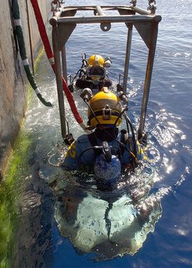 US Navy (USN) divers assigned to Mobile Diving and Salvage Unit One (MDSU-1) and Japanese Self Defense Force divers, are lowered into the waters off the coast of Hawaii, by crewmembers aboard the Crowley 450-10 barge, during recovery operations for the Japanese fishing vessel Ehime Maru