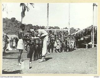 TAMKAIDAN, NEW BRITAIN. 1945-01-15. VX62790 CAPTAIN H.L. (LES) WILLIAMS, MC, ALLIED INTELLIGENCE BUREAU GIVING NATIVES INJECTIONS FOR YAWS AND FRAMBOESIA. STANDING ON THE LEFT IS SERGEANT COLMAN ..