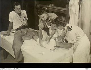 Port Moresby, New Guinea. 1944-05-09. Nursing sister or physiotherapist VFX138546 Lieutenant M. Chalmers (right) assisted by SX39492 Lieutenant W. Hames (centre) applying a plaster and a walking ..