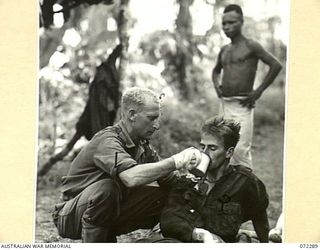 YAULA, NEW GUINEA. 1944-04-10. VX143638 SERGEANT K. LOCKHART (1), GIVES A DRINK TO VX108664 CORPORAL E. ANTHERSON, 57/60TH INFANTRY BATTALION (2), AT THE BATTALION'S FORWARD REGIMENTAL AID POST