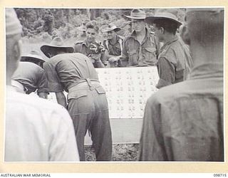 MISSION POINT, NEW GUINEA. 1945-11-09. AUSTRALIAN TROOPS ASSISTING THE WAR CRIMES COMMISSION EXAMINE PHOTOGRAPHS OF SUSPECTED JAPANESE WAR CRIMINALS ARRANGED ON A PANEL