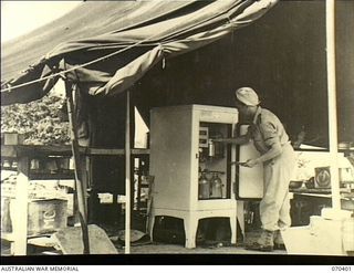 FINSCHHAFEN, NEW GUINEA, 1944-01-31. VFX59385 SISTER L. RAE, AUSTRALIAN ARMY NURSING SERVICE (AANS), 2/3RD CASUALTY CLEARING STATION, EXAMINING THE CONTENTS OF A KEROSENE REFRIGERATOR WHICH USUALLY ..