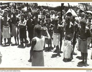 HOPOI, NEW GUINEA, 1943-10-20. A NATIVE INTERPRETER TRANSLATING THE ADDRESS OF NX155085 CAPTAIN R.G. ORMSBY OF THE AUSTRALIAN AND NEW GUINEA ADMINISTRATIVE UNIT TO THE VILLAGE NATIVES