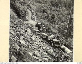 ZENAG, NEW GUINEA, 1944-02-27. A JEEP AND TRAILER CONVOY CONTINUING ALONG THE ROAD FOURTY EIGHT AND A HALF MILES FROM WAU AFTER THE SURFACE HAD BEEN CLEARED FROM A LANDSLIDE BY A D6 ANGLE DOZER ..