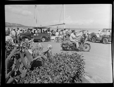 Street scene with police officer on motor bike, people standing watching a passenger boat go past, Papeete, Tahiti