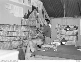 PIVA AIRSTRIP, JACQUINOT BAY, NEW BRITAIN, 1945-07-17. SGT H.N. WHITCOMBE (1), AND CPL D.C. O'HALLORAN (2), RNZAF STAFF ENGAGED IN MAKING UP A MOSAIC OF THE GAZELLE PENINSULA FOR THE PLANNING OF ..