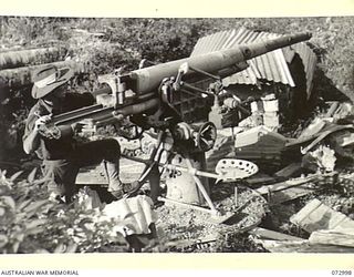 MADANG, NEW GUINEA. 1944-04-25. AN AUSTRALIAN LIEUTENANT STANDS ALONGSIDE A BOMB DAMAGED JAPANESE 75MM FIELD ANTI-AIRCRAFT GUN MOUNTED NEAR THE WATERFRONT. THIS GUN WAS MOBILE AND WAS USED ..