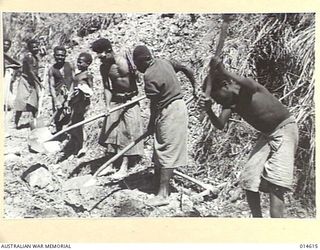 1943-04-08. NEW GUINEA. A NATIVE CHILD SMILES AS OTHERS CONSTRUCT A NEW ROAD, FOR MILITARY PURPOSES IN NEW GUINEA. (NEGATIVE BY F. BAGNALL)
