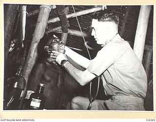 NEW GUINEA. 1942-08. CAPTAIN P. JENSEN, COMMANDING OFFICER OF NATIVE MEDICAL SERVICES IN NEW GUINEA EXAMINES A NATIVE FOR A THROAT COMPLAINT