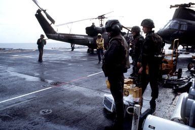 Flight operations take place abord the amphibious assault ship USS GUAM (LPH 9) as it cruises near Grenada during Operation URGENT FURY. Visible in the background is the tail of a UH-1 Iroquois helicopter and the front of a CH-46 Sea Knight helicopter