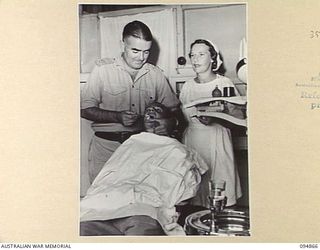 LAE AREA, NEW GUINEA. 1945-08-11. MAJOR B.J. MAHON, DENTAL OFFICER (1), ASSISTED BY PRIVATE E.C. REILLY, DENTAL ORDERLY (3), GIVING TREATMENT TO E. SMITH (2), AT 2/7 GENERAL HOSPITAL