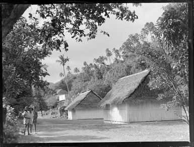 Three unidentified local girls near two huts, Rarotonga, Cook Islands, including tall palm trees in the background