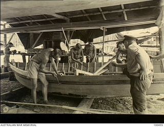 Yule Island, New Guinea. c. 1944-05-15. Members of 1 Marine Food Supply Platoon working on a dinghy at the unit HQ. Left to right: Private (Pte) Morton; Pte Tibbetts; Pte Banard; George English; ..