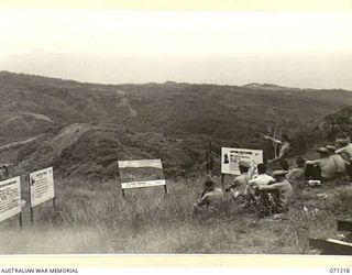 FINSCHHAFEN AREA, NEW GUINEA, 1944-03-17. VX5104 MAJOR V.J. SCHOFIELD, GENERAL STAFF OFFICER II, LIAISION OFFICER OF THE 2ND AUSTRALIAN CORPS POINTS OUT FEATURES OF TERRAIN TO OBSERVERS ON ..