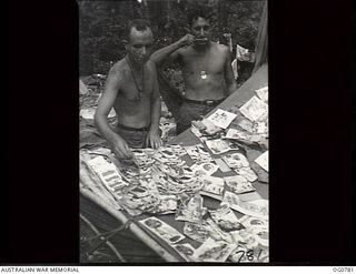 MOMOTE, LOS NEGROS ISLAND, ADMIRALTY ISLANDS. 1944-03-18. BARE-CHESTED RAAF AIRMEN LEADING AIRCRAFTMAN (LAC) D. E. QUANE, MOSMAN, NSW, DRIES OUT A COLLECTION OF JAPANESE LEAFLETS WHILE LAC A. R. ..
