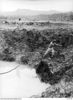 ALEXISHAFEN, NEW GUINEA. 1944-05-11. MEMBERS OF A RMSU (RENDERING MINES SAFE UNIT) RAN, EXAMINING A LARGE CRATER AT THE ALEXISHAFEN NO.1 AIRSTRIP. THE CRATER IS BELIEVED TO HAVE BEEN CAUSED BY THE ..